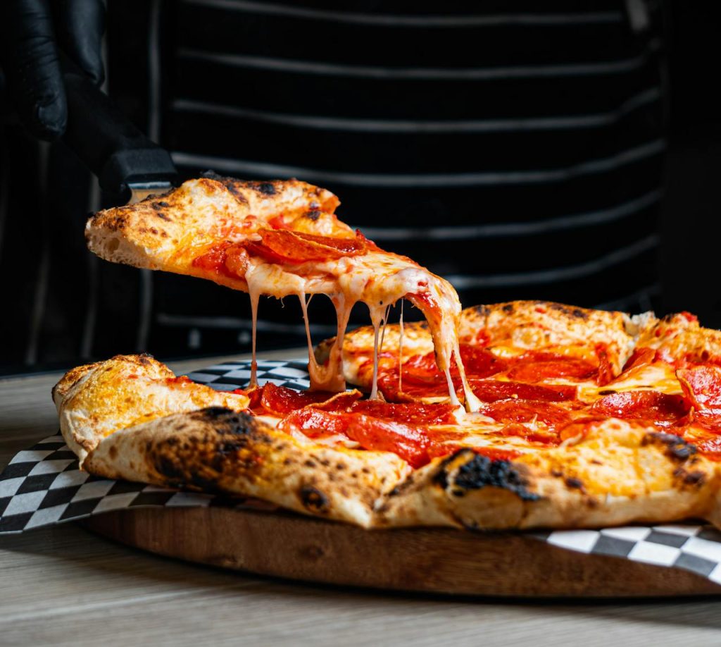 delicious-pepperoni-pizza-slice-being-served-29605927 Close-up of a cheese-laden pepperoni pizza with a slice being served, ideal for food enthusiasts.